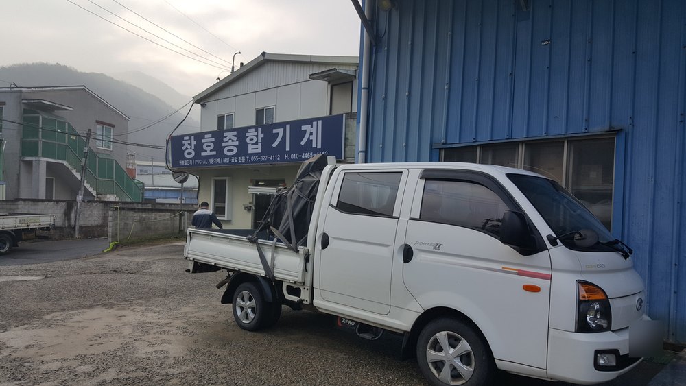 「창호종합기계」 간판 앞에 선, 덮개를 씌운 트럭